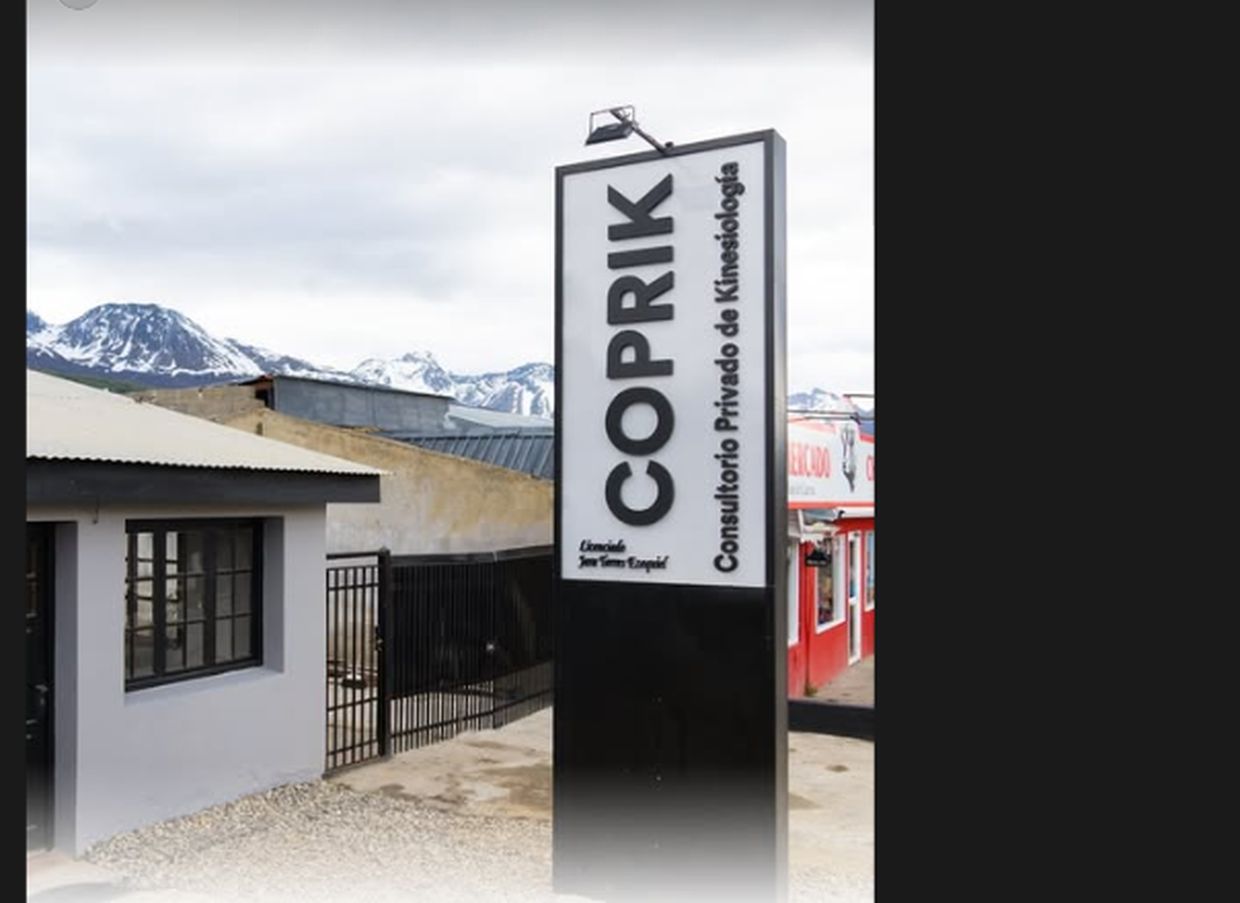 Frente del consultorio COPRIK con su cartel vertical, casa blanca y montañas nevadas detrás